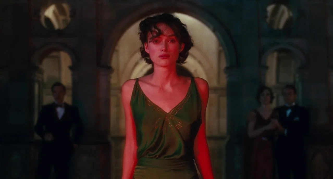 Atonement (2007) movie still: medium — A dimly lit grand interior with stone arches and guests in formal attire. A woman stands in the center…