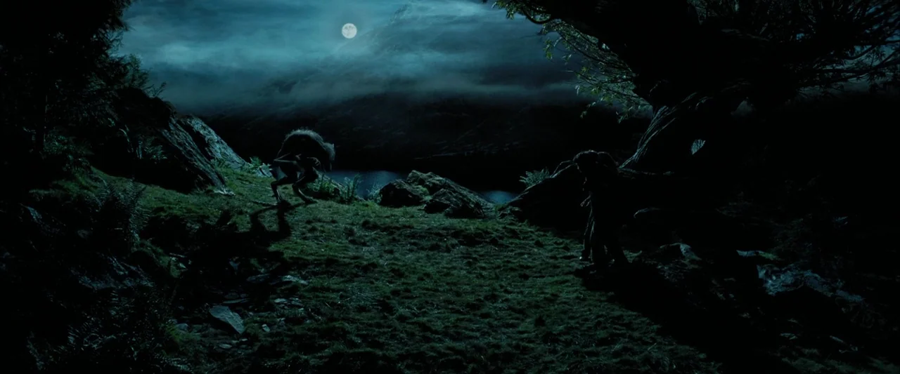 Harry Potter and the Prisoner of Azkaban (2004) movie still: wide — A grassy clearing sits between a dark lake and mountainous hills under a moon. A…