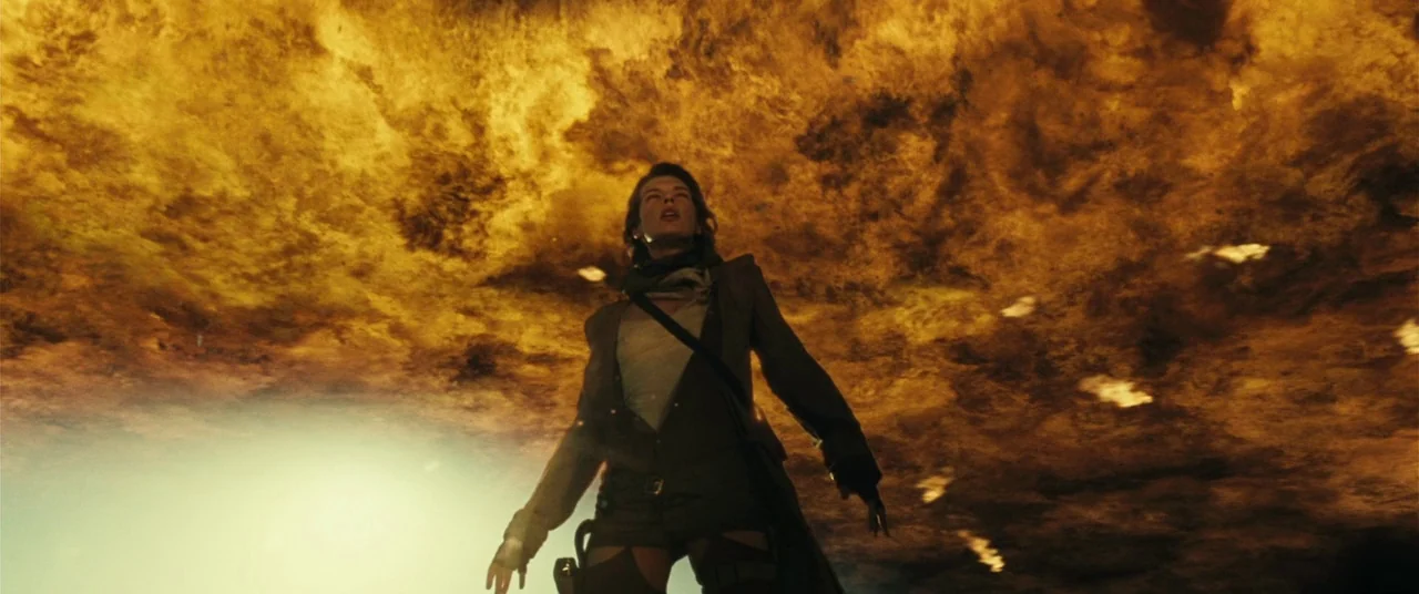 Resident Evil: Extinction (2007) movie still: fullbody — A character stands in a desolate landscape beneath a swirling, fiery orange storm sky. She…