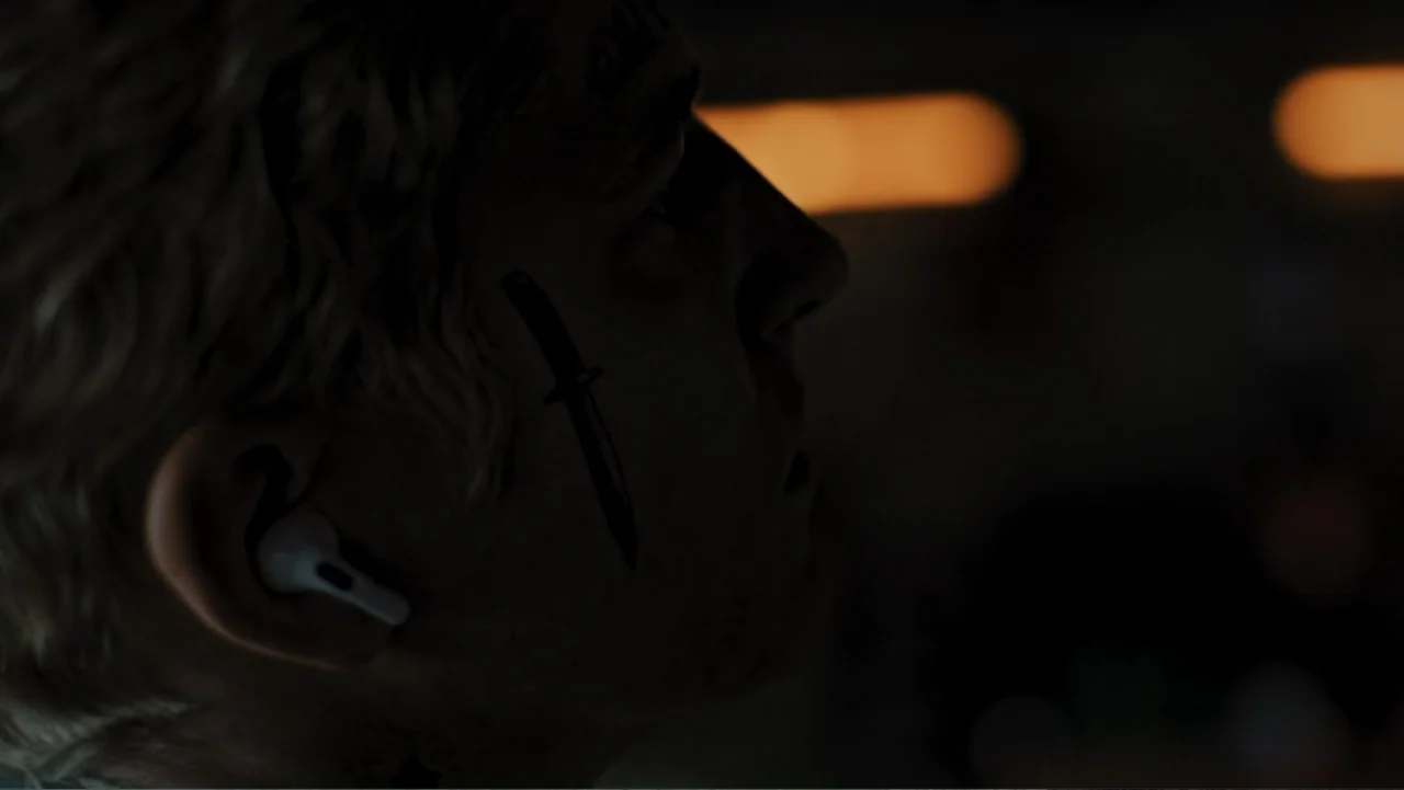 Bullet Proof (2022) movie still: closeup — A dimly lit room with out-of-focus warm light sources in the background. A man with a knife tattoo on his…