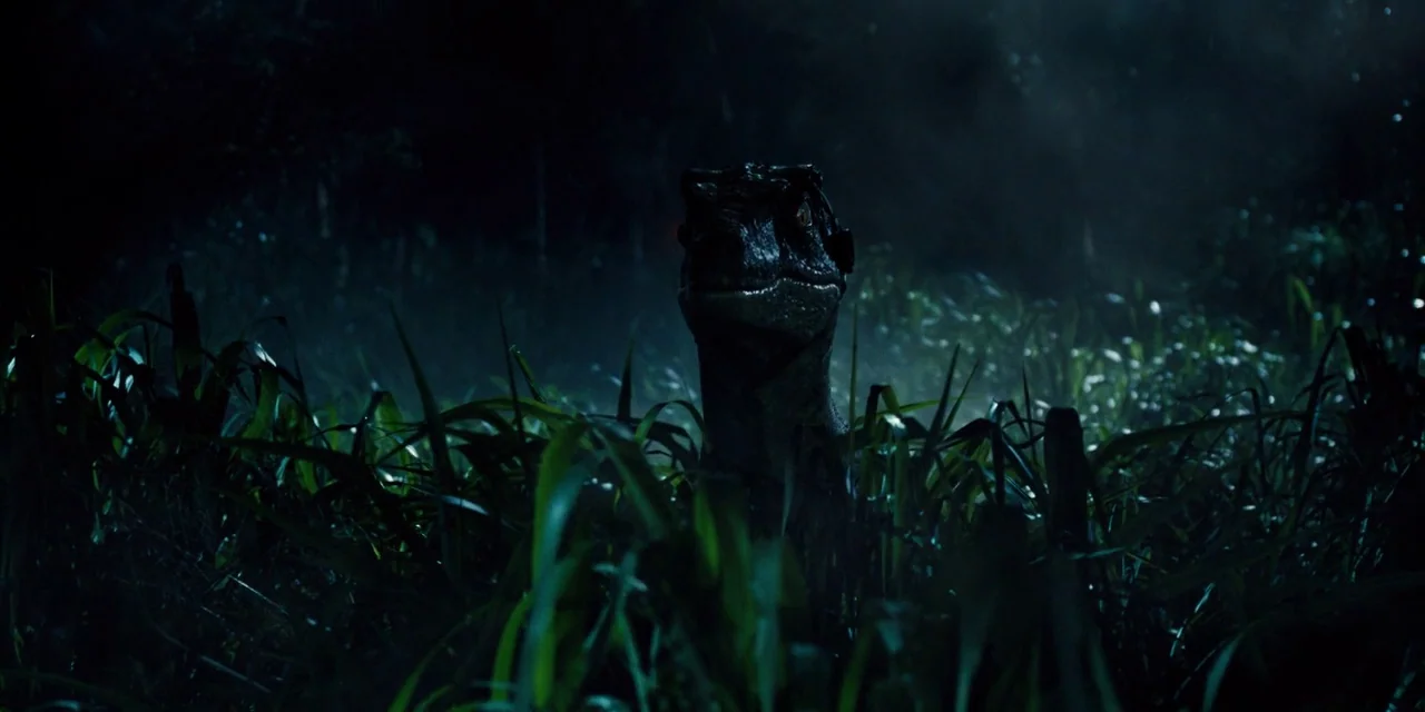 Jurassic World (2015) movie still: medium — A dark, dense grassland environment at night with tall blades of grass everywhere. A dinosaur head…