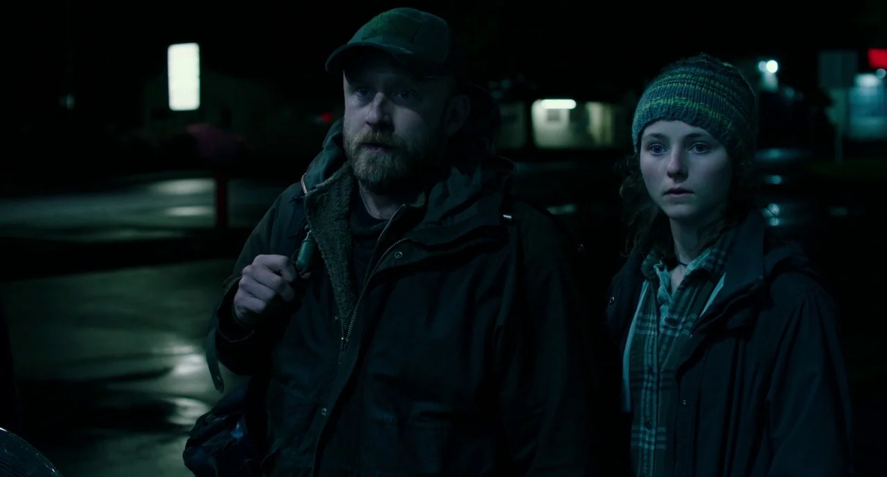 Leave No Trace (2018) movie still: medium — Two individuals stand in a dark, paved area at night under cool lighting. A man and a young woman look…
