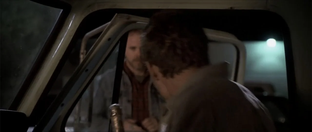 Joy Ride (2001) movie still: medium — Inside a pickup truck at night, a man stands outside the open passenger door. The driver in the foreground is…