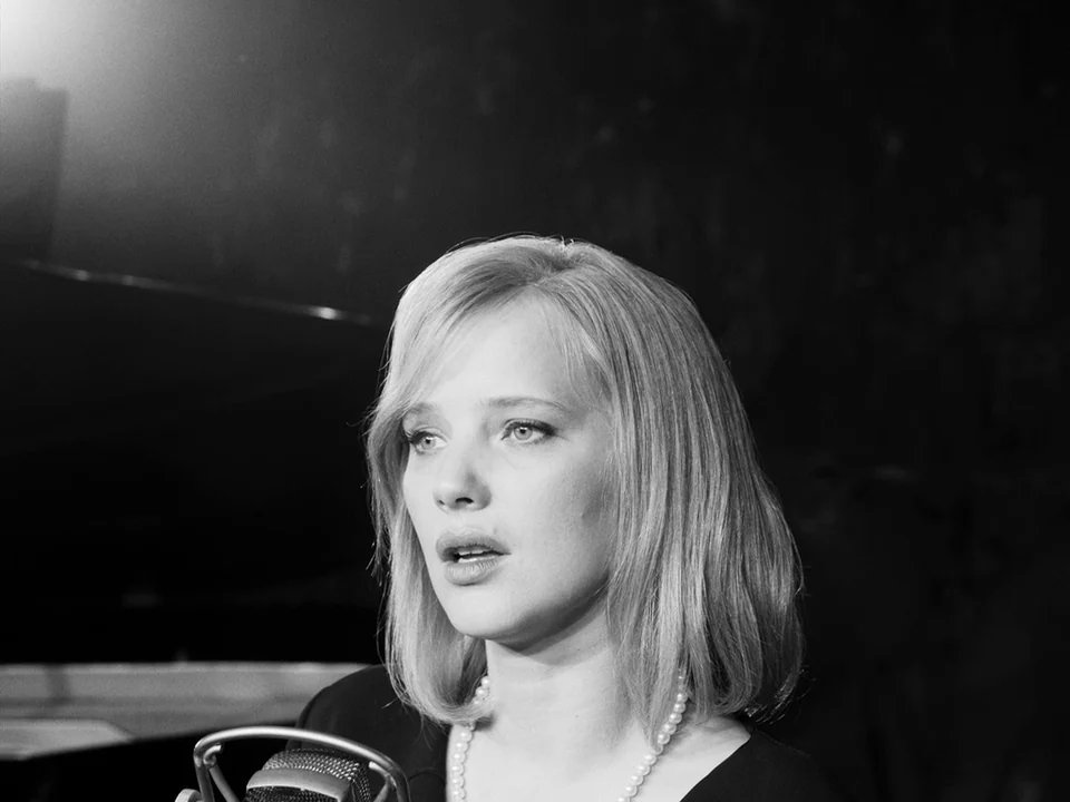 Cold War (2018) movie still: closeup — A dark, dimly lit studio space with a microphone visible in the foreground. A blonde woman sings in front of…