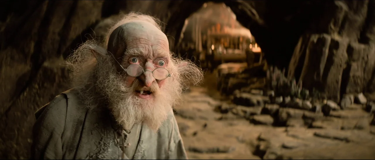 The NeverEnding Story (1984) movie still: medium — A dimly lit rocky cavern with uneven stone ground and dark wall recesses. An elderly goblin-like…