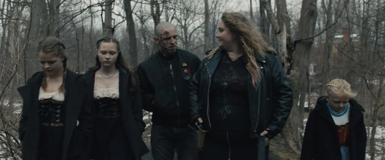 Skin (2009) movie still: medium — A group of five people walks along a narrow trail surrounded by winter woodland. The people are dressed in dark…
