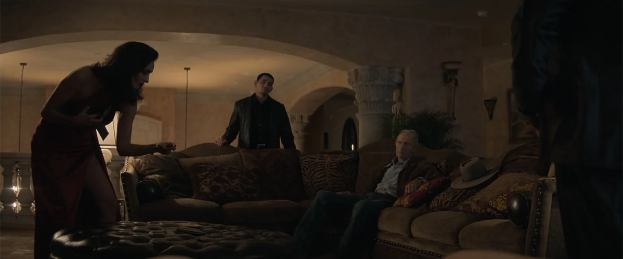 Cry Macho (2021) movie still: medium — A spacious high-end interior featuring ornate stone columns and deep brown upholstered furniture. A woman in…