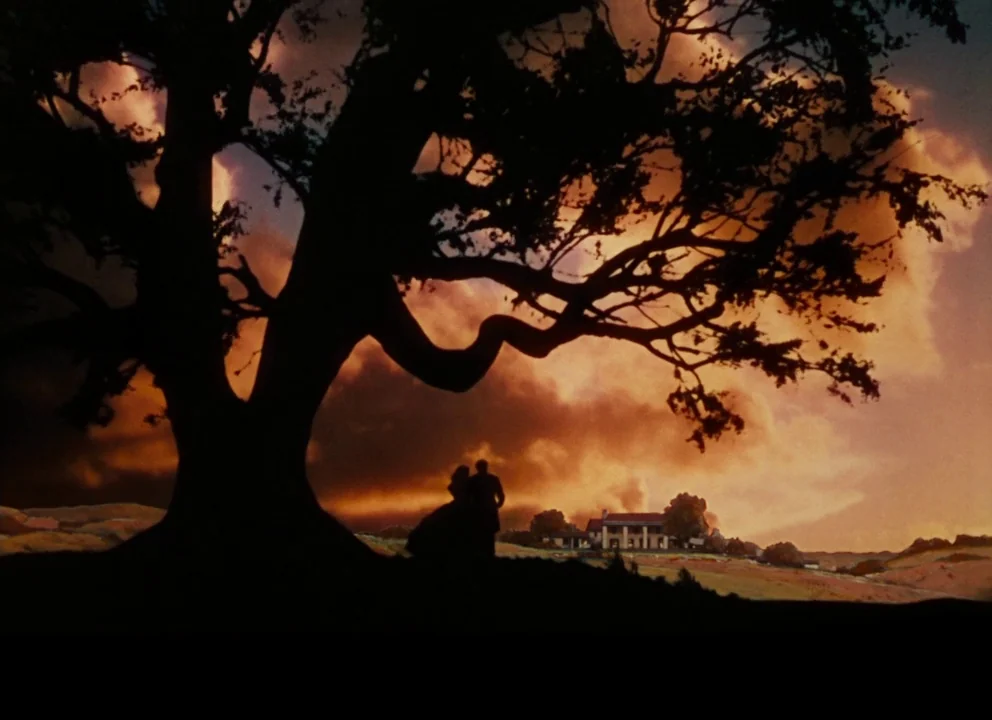 Gone with the Wind (1939) movie still: wide — A sprawling grassy landscape contains a massive, dark, sprawling oak tree in the foreground. A man and…