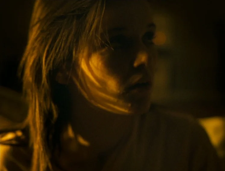 Fish Tank (2009) movie still: closeup — A dimly lit room provides a dark background to a person's face. The subject turns their head slightly while…