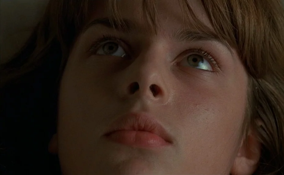 To The Devil a Daughter (1976) movie still: closeup — A close-up view focuses on a teenager's face set against a plain background. The subject lies…