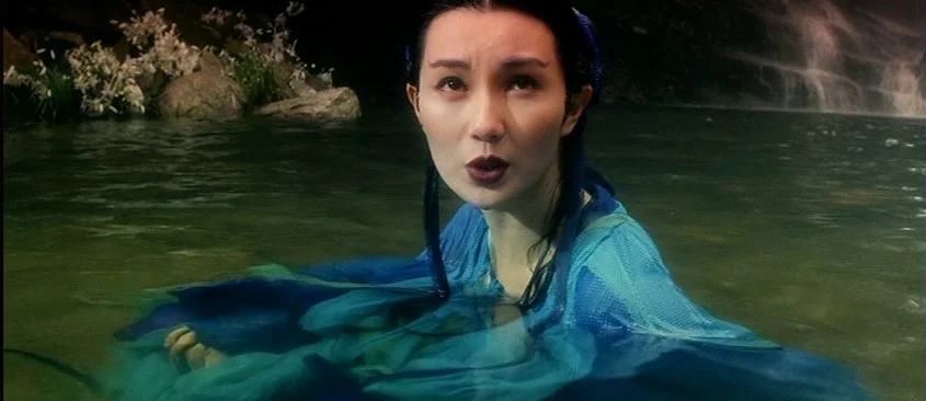 Green Snake (1993) movie still: medium — A woman stands chest-deep in a clear shallow pool near a small waterfall. Large rocks and white flowering…
