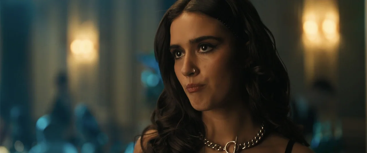 My Fault: London (2025) movie still: closeup — A dimly lit indoor space with out-of-focus background lights suggesting a large gathering. A young…