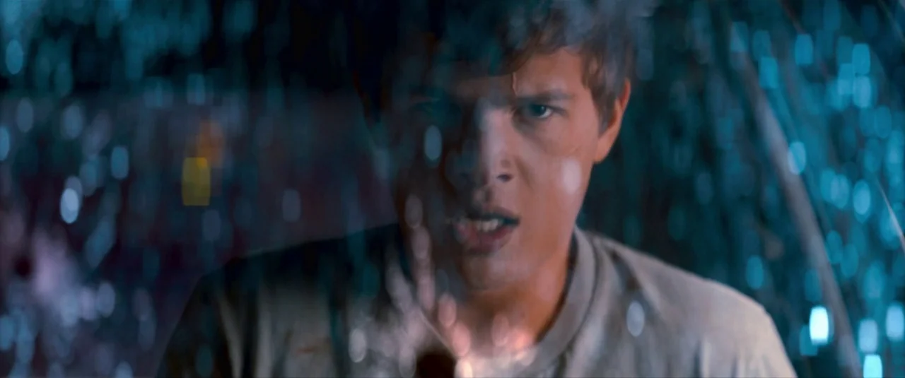 Baby Driver (2017) movie still: closeup — A man looks through rain-covered glass at night in an urban environment. Out of focus street lights appear…