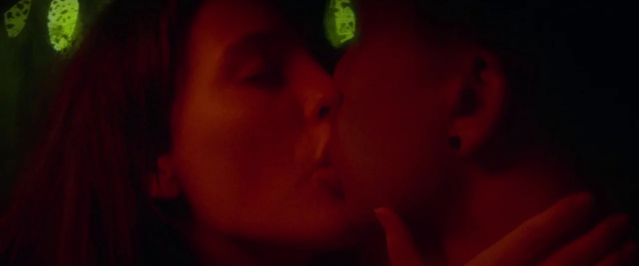 Kissing Candice (2017) movie still: closeup — A couple kisses in a dark interior space illuminated by red neon lighting. Green decorative patterns…