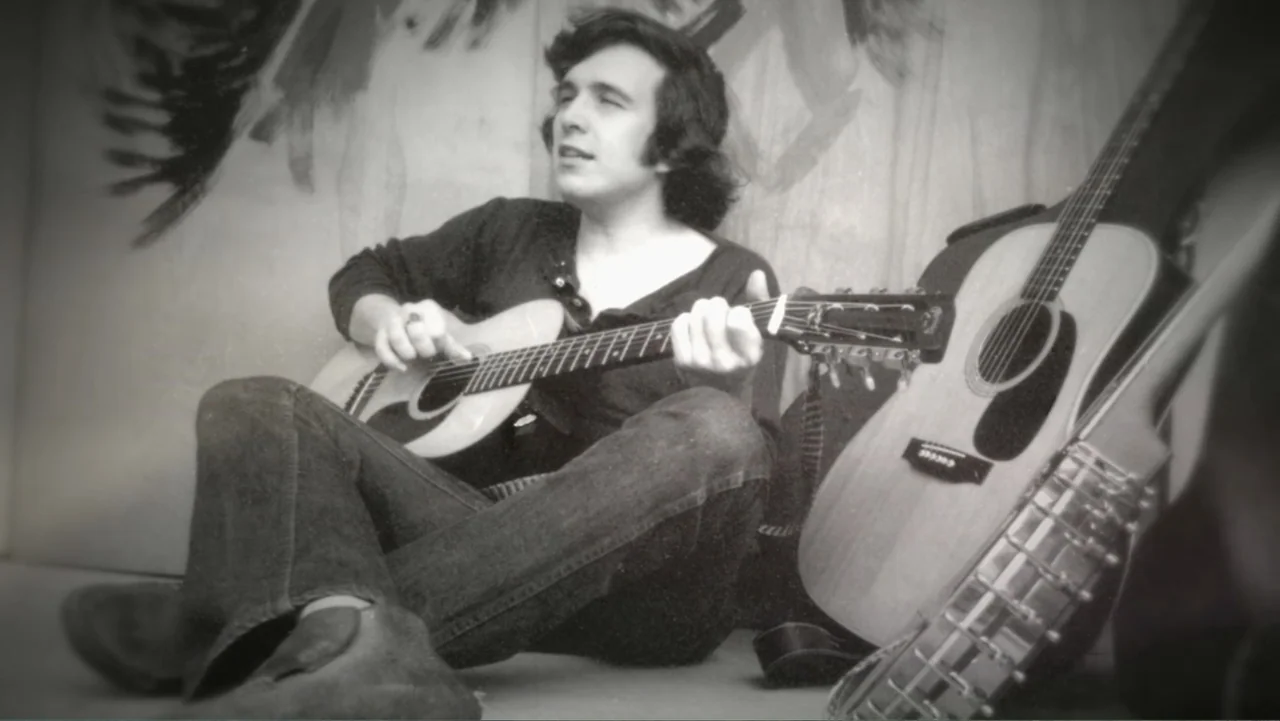 The Day the Music Died: The Story of Don McLean's "American Pie" (2022) movie still: medium — A man sits on the floor inside a room with simple…