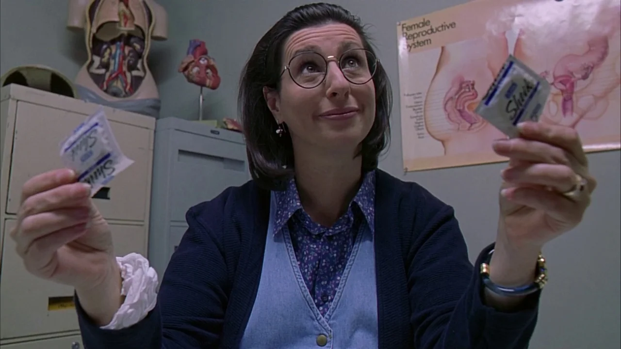 Ginger Snaps (2000) movie still: medium — A clinical office room features medical anatomy posters and a torso model on top. A woman wearing glasses…