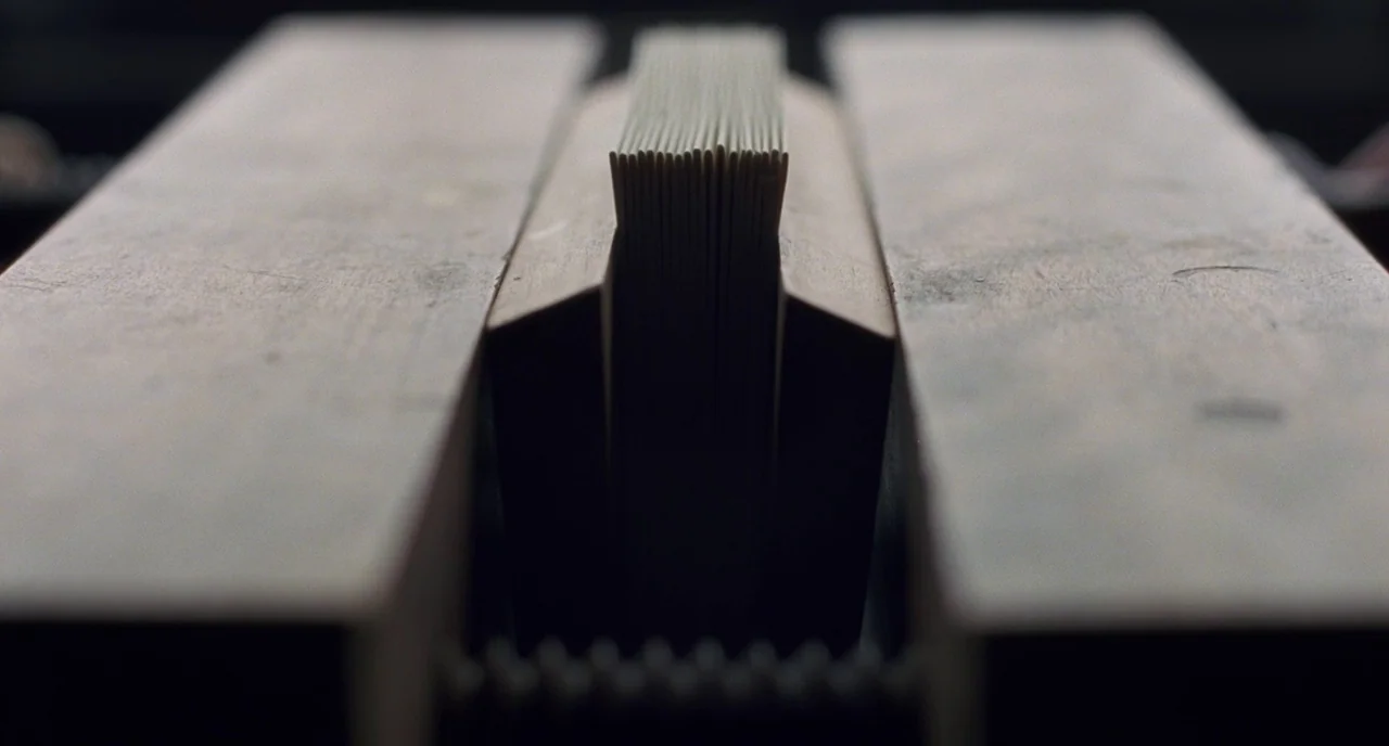 Little Women (2019) movie still: closeup — A thick stack of paper is held vertically between two heavy, weathered wooden blocks. The wooden press…
