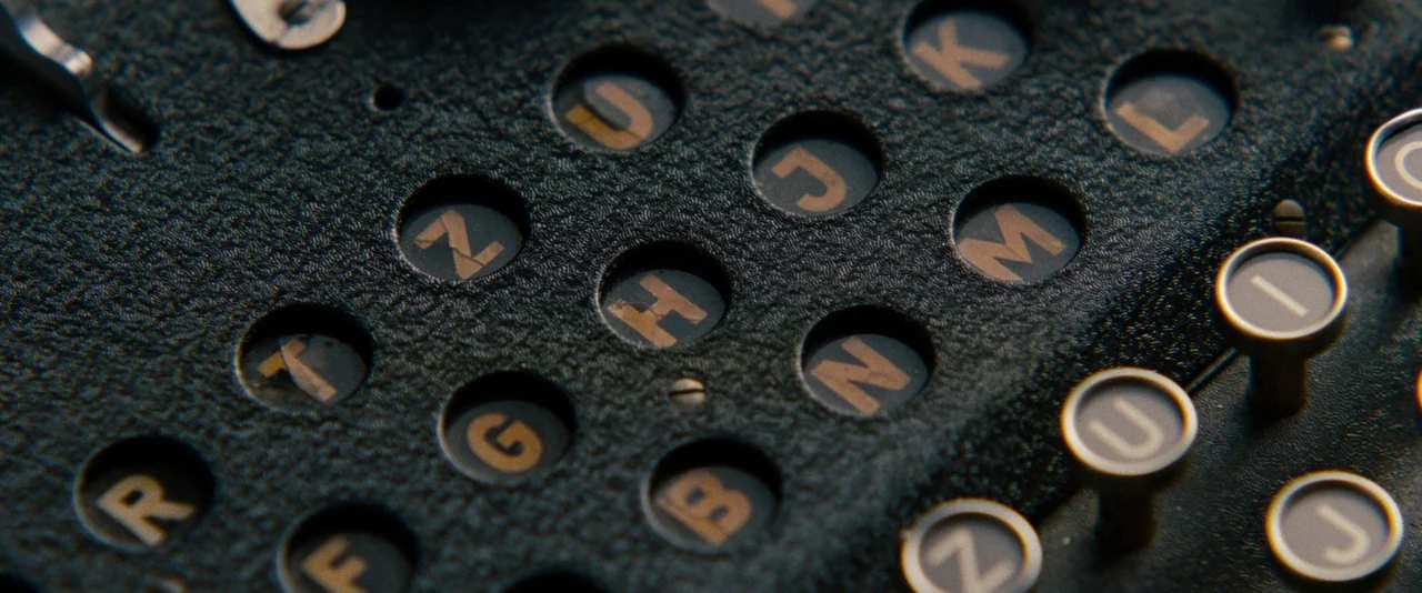 The Imitation Game (2014) movie still: closeup — A close-up view of a vintage Enigma machine showing worn lettered keys and sockets. The black…