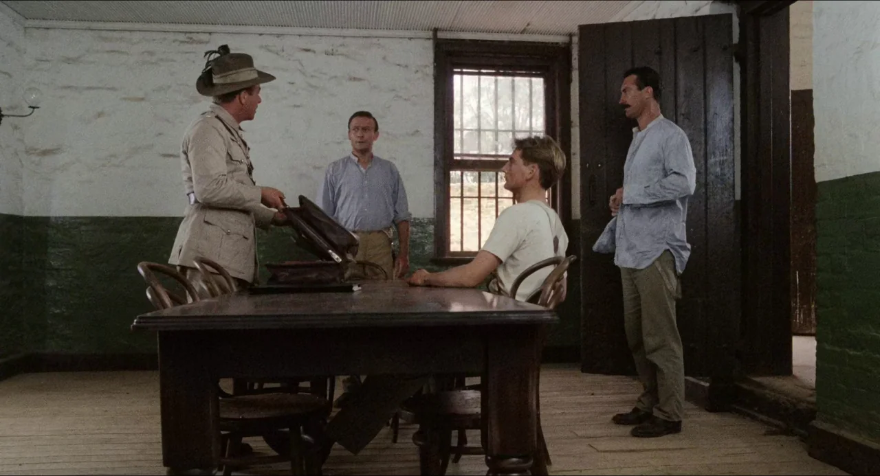Breaker Morant (1980) movie still: fullbody — An austere room with white-washed brick walls and a dark green painted baseboard. Four men stand…