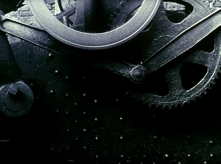 Daisies (1966) movie still: closeup — Massive cast iron machine parts are arranged in a dark industrial environment. Interlocking gears and metal…