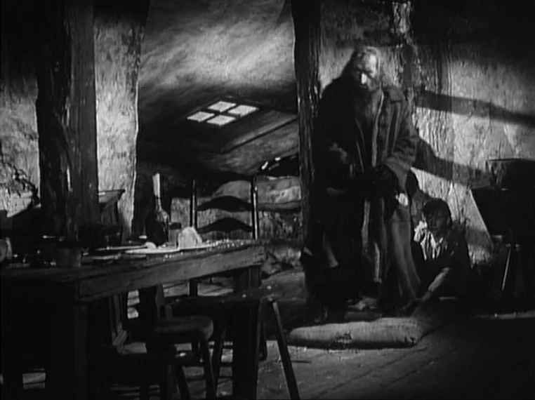 Oliver Twist (1948) movie still: fullbody — An interior space with wooden support beams and a rectangular roof window opening. An older man stands…