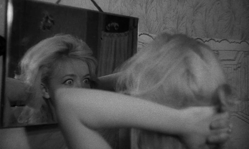 Man Is Not Bird (1965) movie still: closeup — A woman stands before a wall mirror with patterned wallpaper in the background. She is seen from…