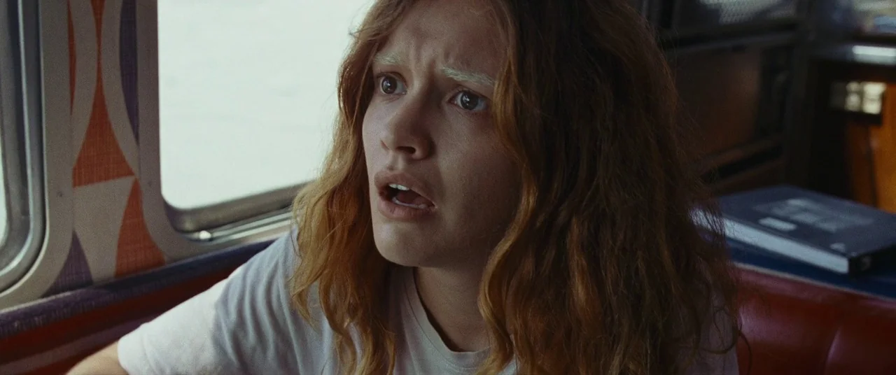 Sound of Metal (2019) movie still: closeup — A passenger seat inside a vehicle with patterned window curtains and red vinyl upholstery. A young…