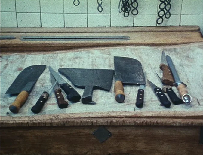 Daguerréotypes (1976) movie still: closeup — A collection of assorted steel butcher knives and cleavers rests on a heavy wooden surface. White tiles…