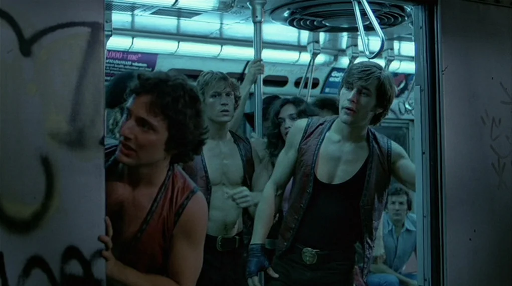 The Warriors (1979) movie still: medium — A crowded subway car at night features faded advertisements on the walls and metal poles. Several young…