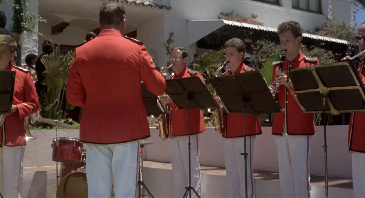 American Ninja 2: The Confrontation (1987) movie still: fullbody — A sunny outdoor patio features a musical ensemble dressed in red formal uniforms.…