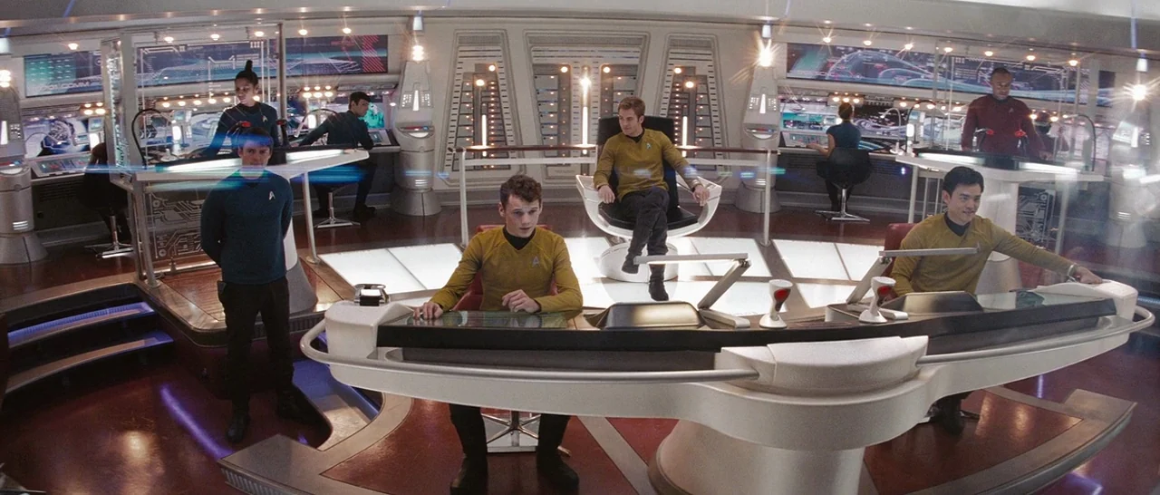 Star Trek (2009) movie still: wide — The interior of a high-tech starship bridge features curved consoles and multiple crew stations. Uniformed…