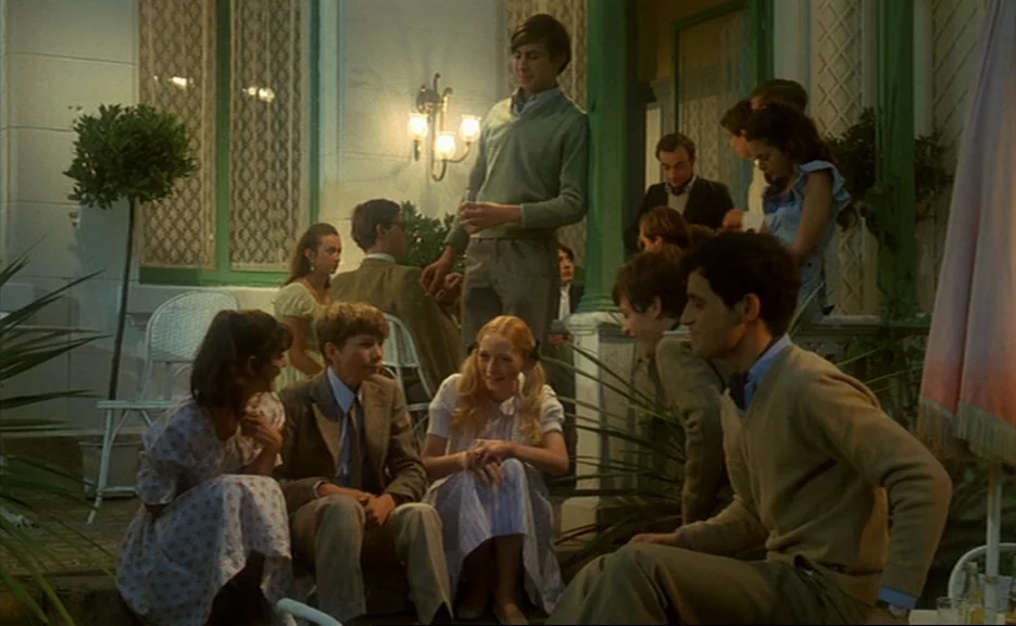 Murmur of the Heart (1971) movie still: medium — A group of adolescents gathers on a decorated exterior terrace at night. Young people sit and stand…