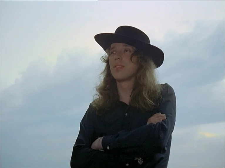 Beware Of A Holy Whore (1971) movie still: medium — An open sky with soft clouds provides a backdrop for a young man. The person stands with arms…