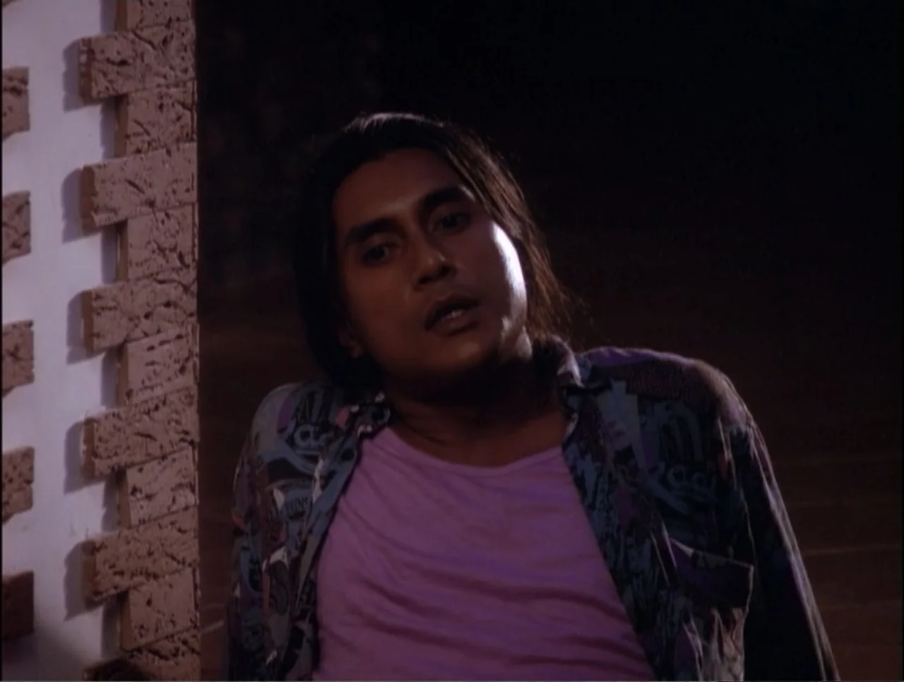 Code Name: Wolverine (1996) movie still: medium — An outdoor area at night featuring a textured white brick pillar on the left. A man in a patterned…