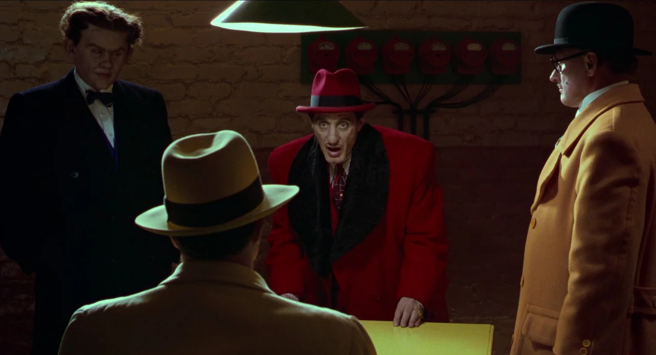 Dick Tracy (1990) movie still: medium — A dimly lit brick basement features four men gathered around a bright yellow table. A man in a vivid red…