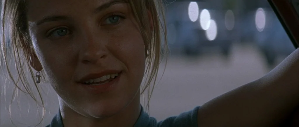 The Underneath (1995) movie still: closeup — A woman sits inside a vehicle at night with blurred city lights visible outside. She looks toward the…