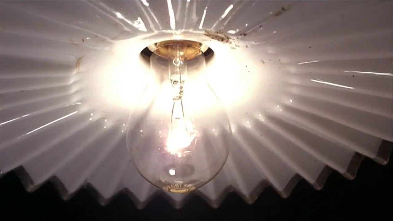 A Quiet Place In The Country (1968) movie still: closeup — A close-up view shows a single lit tungsten lightbulb inside a white fluted shade. The…