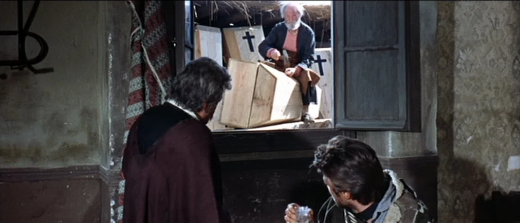 Fistful Of Dollars (1964) movie still: medium — A rustic workshop interior features unpainted wooden coffins stacked near an open window. An elderly…