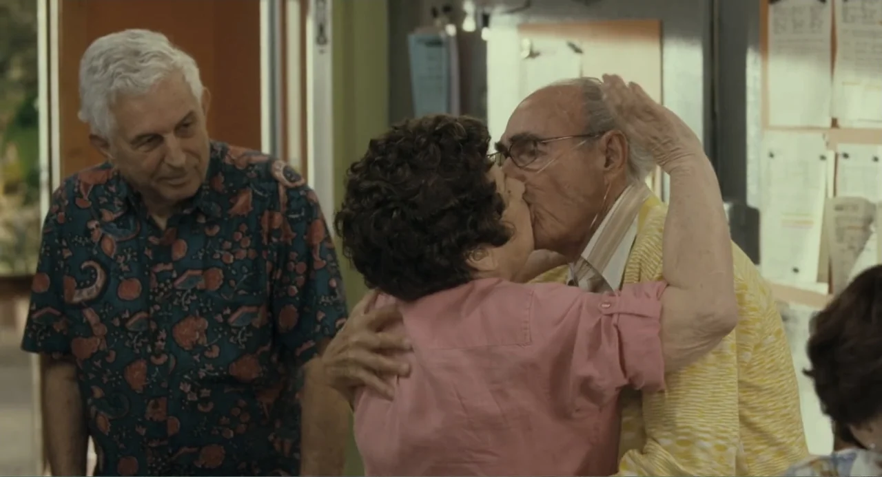 Because I Said So (2007) movie still: medium — A room with light green walls features a notice board covered in papers. An elderly couple embraces…
