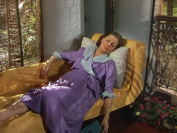 The River (1951) movie still: medium — A woman reclines on a yellow chaise lounge inside a sun-filled, airy room. Light streams through slatted…