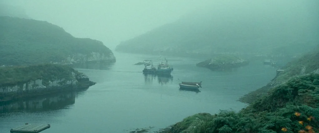 Ondine (2009) movie still: establishing — A quiet coastal inlet is surrounded by low, fog-covered green hills. Two small boats navigate the still,…