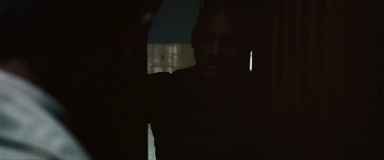 GOMORRAH (2023) movie still: medium — A man stands in a shadowed doorway leading to a brighter room beyond. The man faces forward as he looks at an…