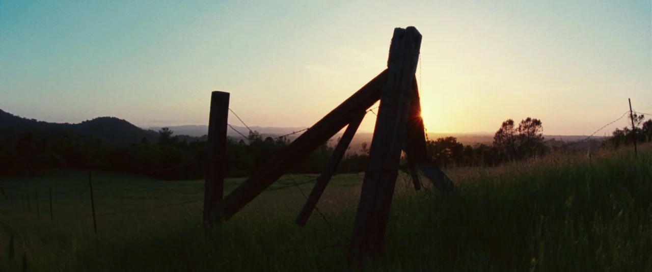 A Hitchhiker’s Guide To The Galaxy (2005) movie still: establishing — A rural pasture features a broken wooden fence illuminated by a setting sun.…