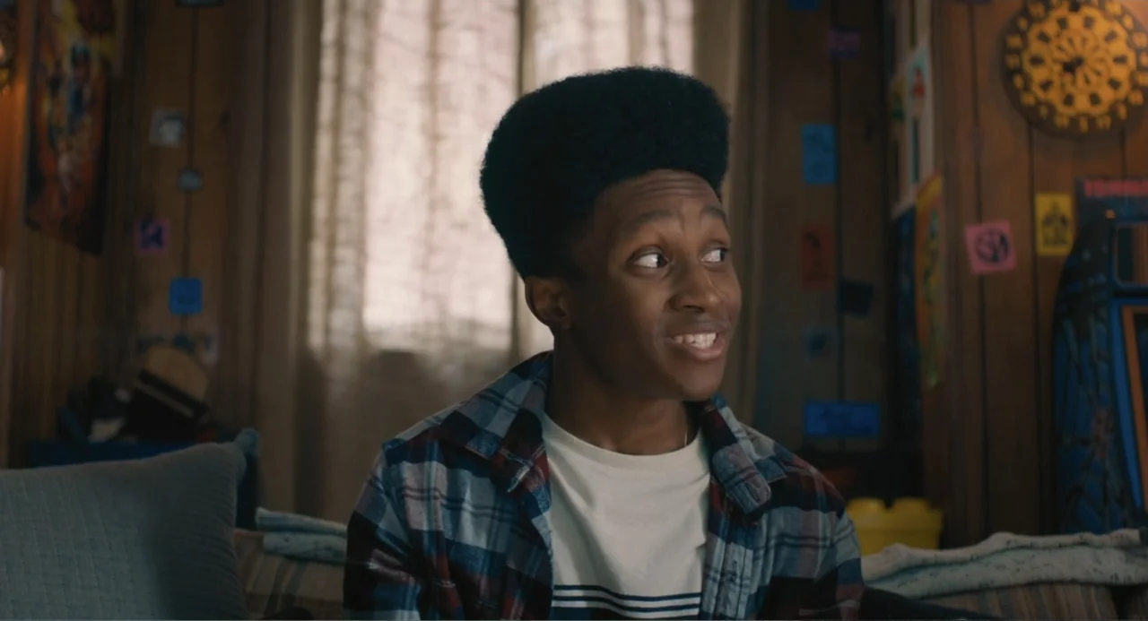 The Map of Tiny Perfect Things (2021) movie still: medium — A wood-paneled room features a window with curtains and wall-mounted decor. A teenage…