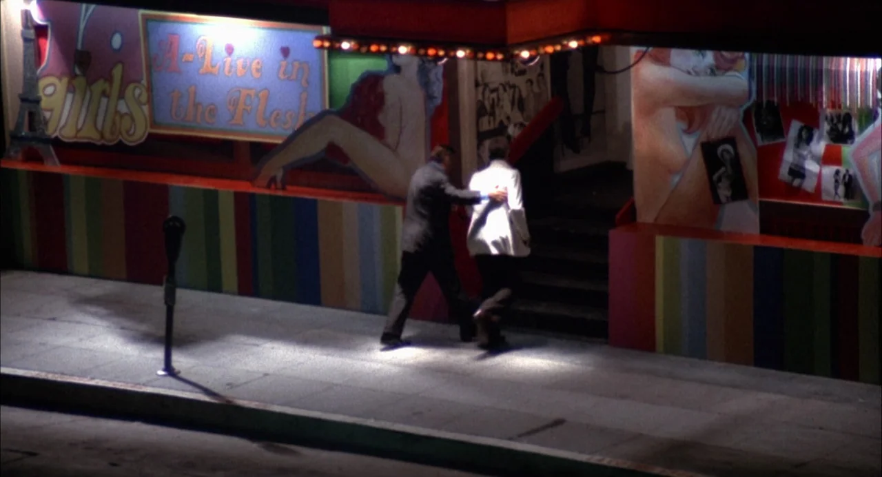 The Killing of a Chinese Bookie (1976) movie still: wide — A dark city sidewalk at night in front of a brightly lit adult venue. Two men in suits…