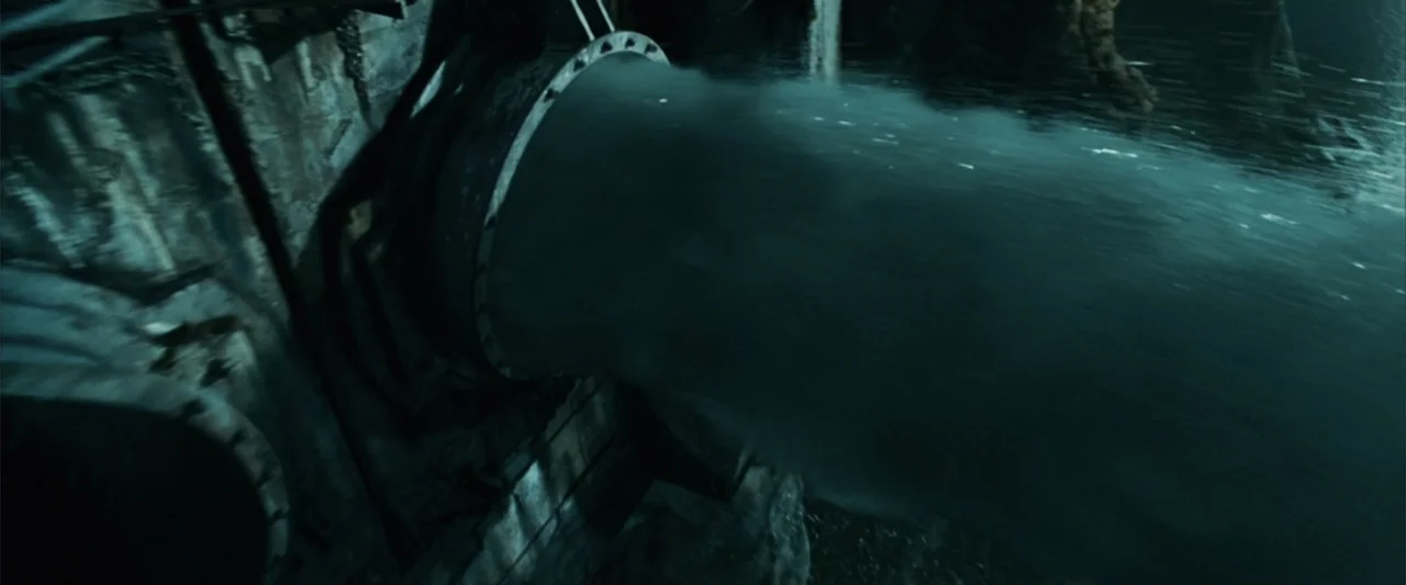 Catwoman (2004) movie still: medium — A rusted industrial pipe discharges a high-pressure stream of water into a dark space. The metallic texture of…