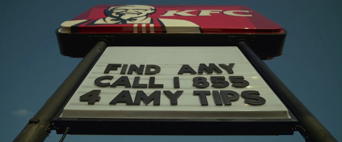 Gone Girl (2014) movie still: closeup — A KFC restaurant sign features a message board asking for tips about a missing person. Black plastic letters…