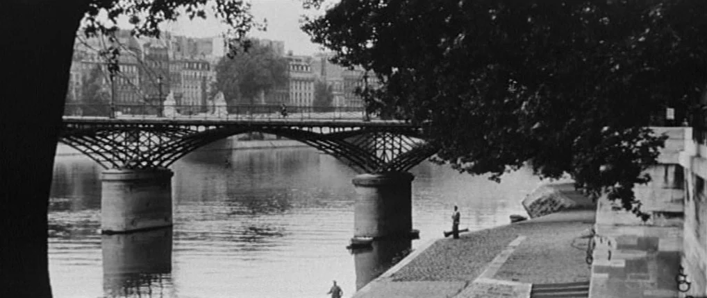 Antoine and Colette (1962) movie still: wide — A stone bridge with ornate metal arches spans a calm river in an urban area. Large trees frame the…