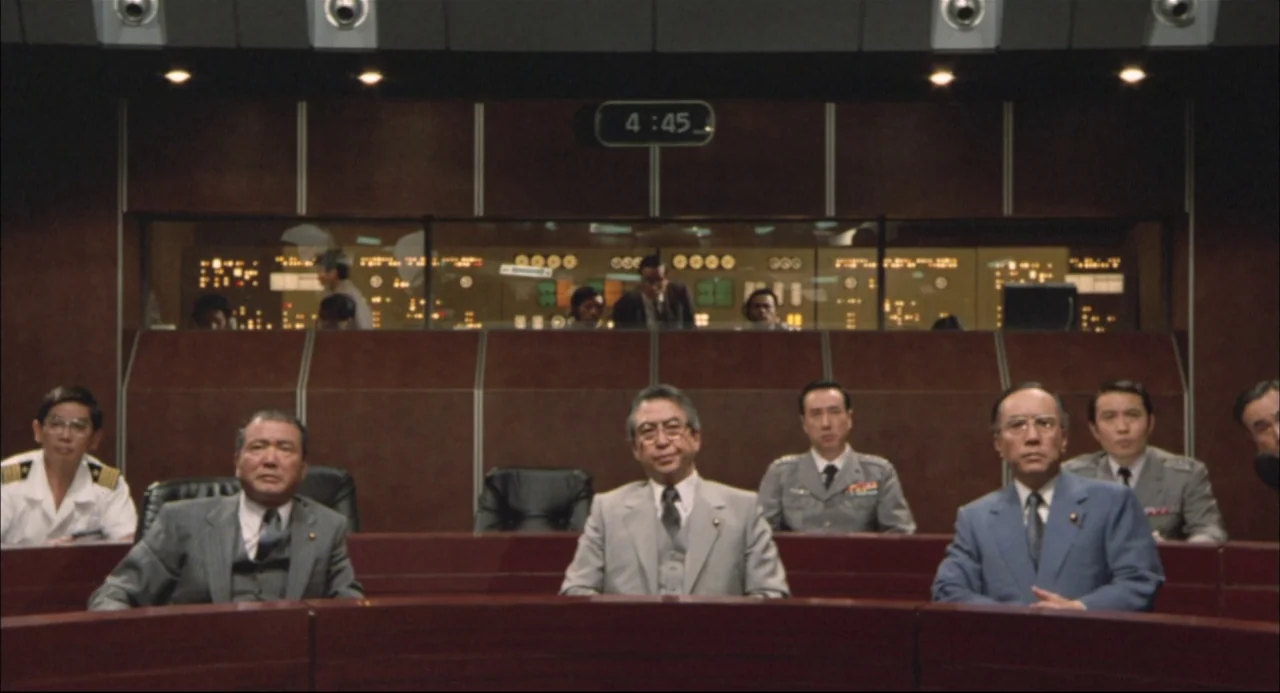 The Return of Godzilla (1984) movie still: wide — A formal government conference room features dark wood paneling and a large observation window.…