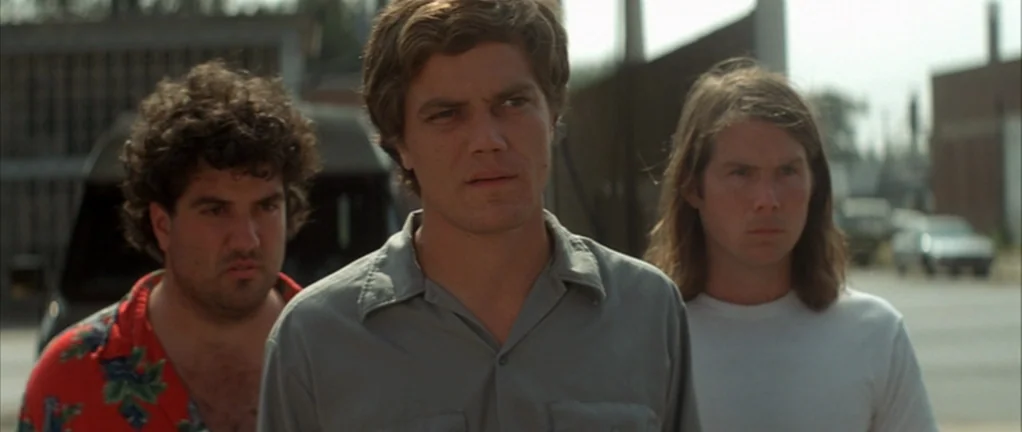 Shotgun Stories (2007) movie still: medium — An outdoor industrial lot with buildings and vehicles in the soft daylight background. Three men stand…
